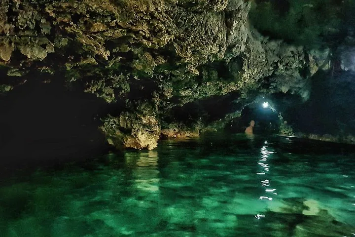 Eine Person watet in klarem, türkisfarbenem Wasser in einer dunklen Höhle.