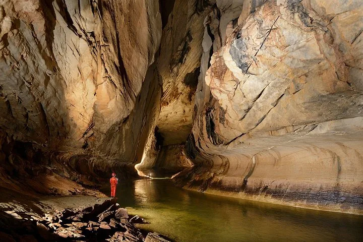 Persona de pie junto a un río subterráneo dentro de una vasta cueva iluminada.