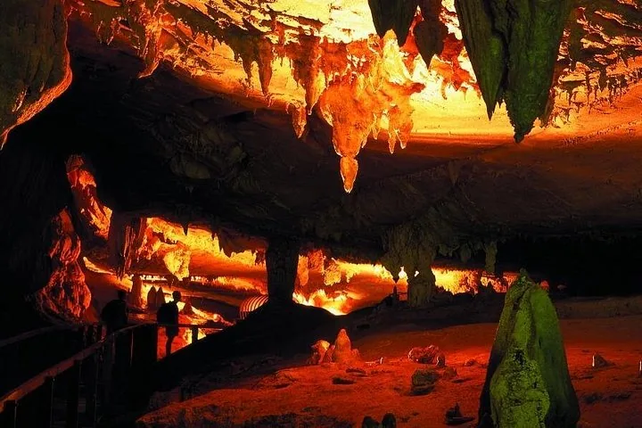 Personas caminando por un sendero dentro de una cueva iluminada con luz naranja.